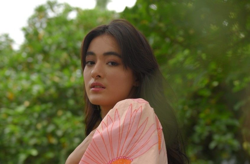 Potret Mawar de Jongh dengan selendang merah muda dan background dedaunan pohon